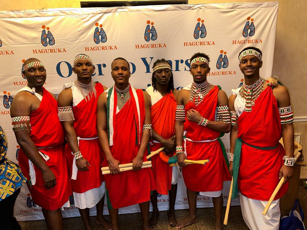 Six drummers in red regalia holding drumsticks at an anniversary event